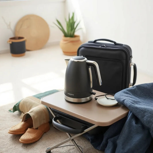 Compact foldable electric kettle on a travel table beside a suitcase and folded mat